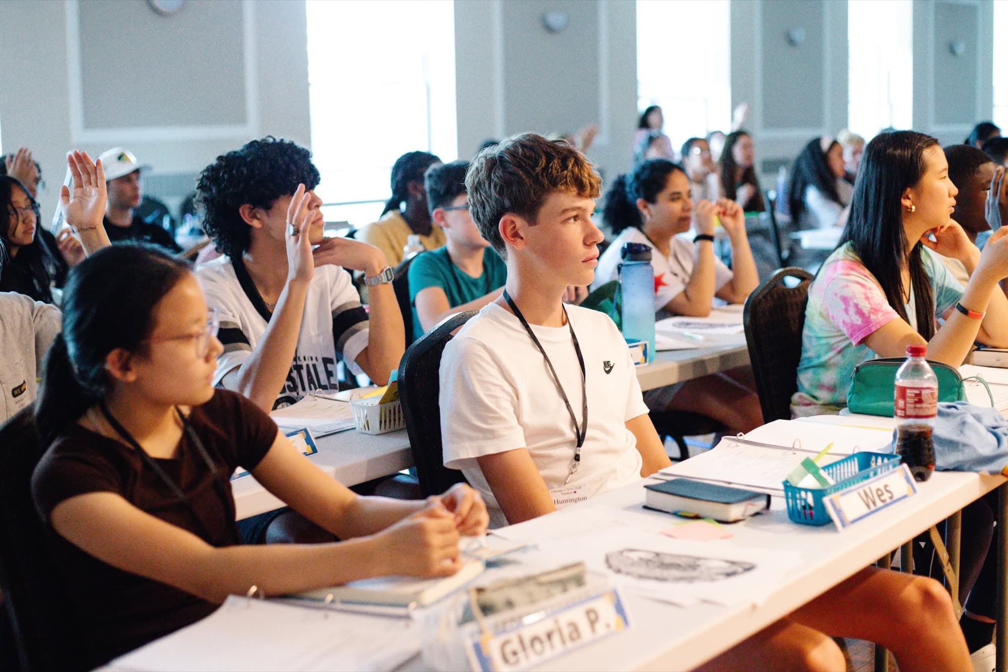 Teenagers wearing name badges sit at tables and listen
